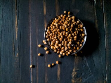 Koyu ahşap yüzeyde kişniş tohumlarıyla dolu küçük cam kase.. 