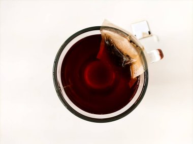 Bir bardak dolusu demlenmiş çay yukarıdan izleniyor. Kehribar renkli bir sıvı, fincanın kenarına kısmen daldırılmış bir çay poşeti..