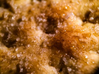 Bisküvinin yüzeyine yakın çekim, altın kahverengisini, çıtır çıtır dokusunu gösteriyor. Şekerin kristalleri tüm yüzeye dağılmış, parlak bir etki yaratıyor..