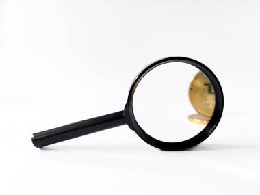 Düz beyaz bir yüzeyde duran siyah bir büyüteç altındaki altın Bitcoin 'e odaklanıyor..