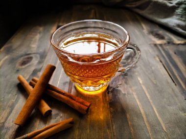 Tarçın çayı içeren şeffaf, karmaşık desenli bir cam bardak kırsal bir ahşap yüzeyde oturur..