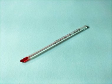 Pastel mavi arka planda kırmızı sıvı göstergesi olan cam termometre..