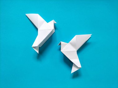 Beyaz origami kuşu kağıttan yapılmış, canlı kırmızı bir arkaplanda sergileniyor.