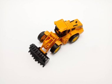 Plastik olarak dizayn edilmiş önyükleyicili sarı oyuncak traktörü, düz beyaz bir arka planda yer almaktadır..
