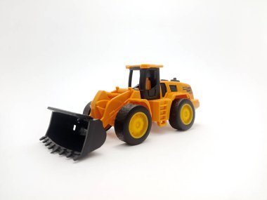 Plastik olarak dizayn edilmiş önyükleyicili sarı oyuncak traktörü, düz beyaz bir arka planda yer almaktadır..