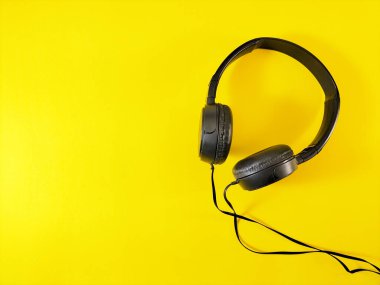 Black headphones with a wired connection are placed on a bright yellow background.