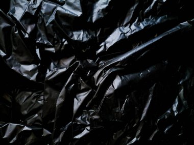 Parlak bir yüzeye sahip buruşuk siyah plastik malzeme, kıvrımlar ve kırışıklıklar ile desenli bir görünüm yaratır..