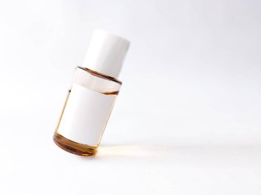 İçinde kehribar sıvısı olan temiz bir cam cilt şişesi beyaz bir yüzeye eğilmiştir..