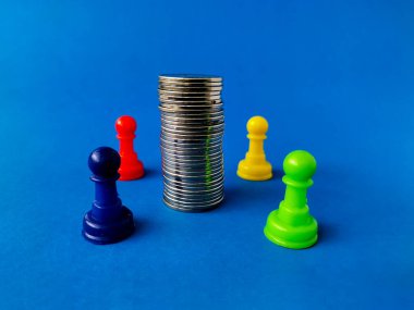 Bir yığın gümüş sikke mavi arka planda dört renkli satranç piyonu ile çevrilidir..