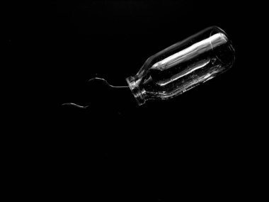 Bir cam şişe eğilmiş, koyu bir yüzeye su döküyor..