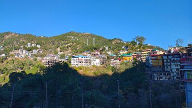 Şehrin panoramik manzarası ve bulutların ve ormanın olduğu mavi gökyüzünün altındaki dağlar parlak ve güneşli bir günde..