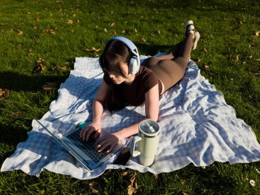 Parkta dizüstü bilgisayarla çalışan genç bir kadın, serbest dijital göçebe yaşam tarzı, açık havada bilgisayarda yazan bir kadın.