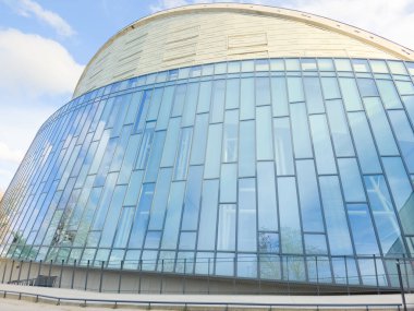 Mavi pencereli ve eğimli mimarisi olan çağdaş ofis binasının modern cam cephesi