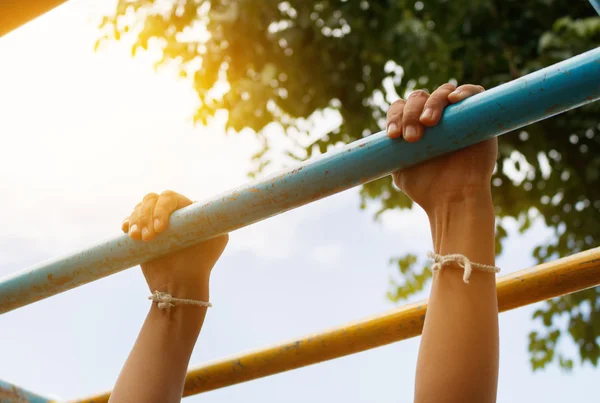 Little boy hanging bar by 2 hands the outdoor exercise equipment in public park, soft focus — Stock Photo, Image