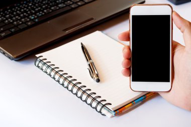 Boş cep telefonu ve hesap makinesi, kalem, dizüstü bilgisayar ile akıllı telefon kullanan bir adam kapatın. Kırpma yolu ile boş ekranlı akıllı telefon. Evde bir masada beyaz akıllı telefon kullanarak el, yumuşak odak.