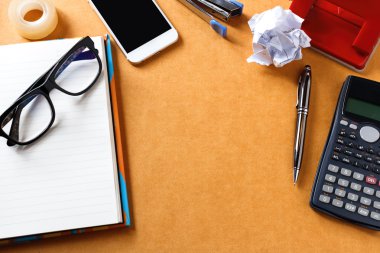 Ahşap ofis ya da masa masasında bir sürü şey var. En iyi görüntü. Not defteri, kalem, gözlük, bant, telefon, zımba, hesap makinesi, buruşturulmuş kağıt, zımba. Bazı metin veya resimler eklenebilir. Yukarıdan kopyalama alanı ve yumuşak odak ile görüntüle.