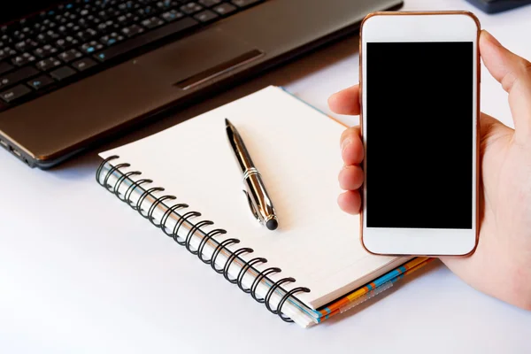 Primer plano de un hombre que utiliza el teléfono inteligente con el móvil en blanco y la calculadora, pluma, portátil. Teléfono inteligente con pantalla en blanco con ruta de recorte. Mano usando un teléfono inteligente blanco en un escritorio en casa, enfoque suave . —  Fotos de Stock