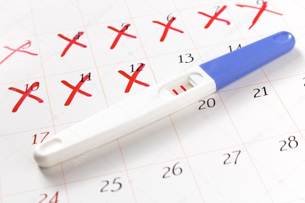 Pregnancy test with positive result lying on calendar