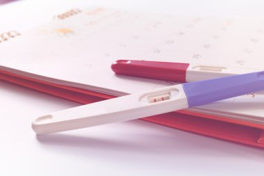 Takvim arka planında pozitif sonuç içeren gebelik testi