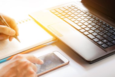 Teknoloji ve ev konsepti, dokunmatik telefon ile el ele yakın, ofiste veri arama ve beyaz masada dizüstü bilgisayar ve dizüstü not almak için cep telefonu kullanın, yumuşak odak.