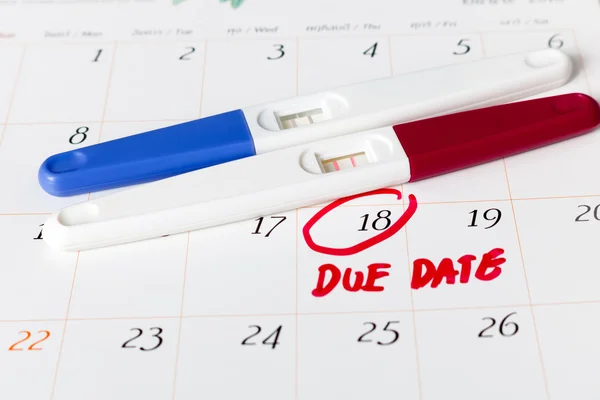 Pregnancy test with positive result lying on calendar background.circle due date 18th, soft focus. — Stock Photo, Image