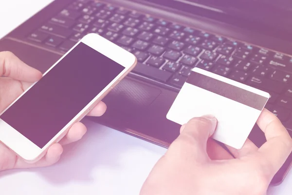 Online-Bezahlung: Die Hände des Mannes halten eine Kreditkarte über den Laptop und nutzen das Smartphone für Online-Einkäufe auf dem Schreibtisch im Büro oder zu Hause — Stockfoto