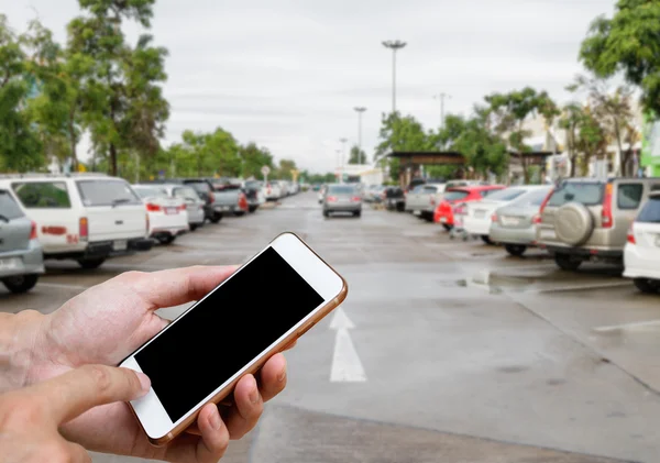 Inteligentny telefon pokazuje pusty ekran w dłoni człowieka z rozmycie samochody parking — Zdjęcie stockowe