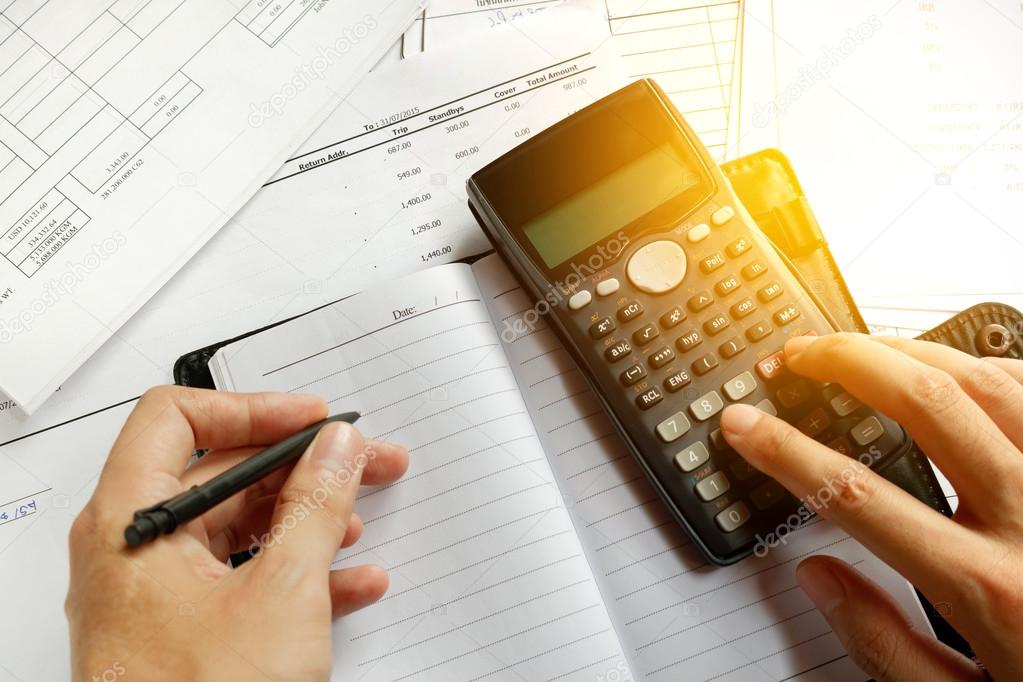 savings, finances, economy and home concept - close up of man with calculator counting making notes at home, hand is writes in a notebook with books, soft focus.
