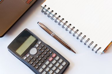 Hesap makinesi ve dizüstü bilgisayarı olan çalışma masası, beyaz masa arkaplanındaki kalem, defter. İş konsepti. Finansal muhasebe. yumuşak odak.
