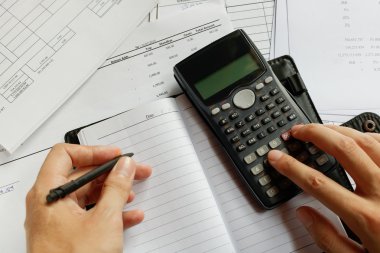 savings, finances, economy and home concept - close up of man with calculator counting making notes at home, hand is writes in a notebook with books, soft focus. clipart