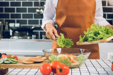 Asyalı kadın salatayı ahşap kesme tahtasına koymak için maşa kullanıyor. Mutfak odasındaki salata kabına..