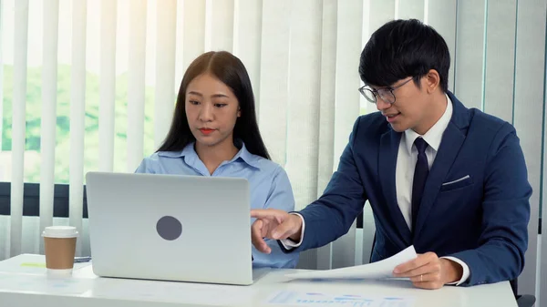 Two asian business people are working together and analyzing the data on the computer.