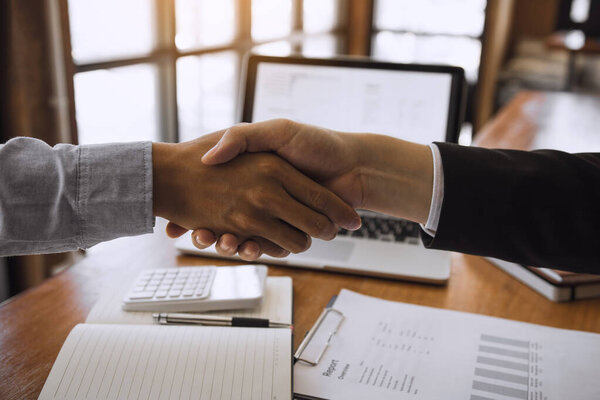 Entrepreneurs collaboration deal shaking hands in a modern office and financial paper graph on desk.