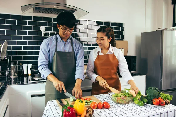 İki genç Asyalı çift birbirine yardım ediyor ve mutfakta yemek pişirmekten zevk alıyorlar..