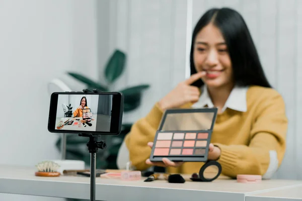 Asian teenage girls doing makeup vlogs and using a video mobile camera to record vlogs and publish them online at home.