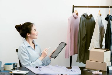 Asyalı girişimci tabletiyle depodaki kalan giysileri kontrol ediyor..