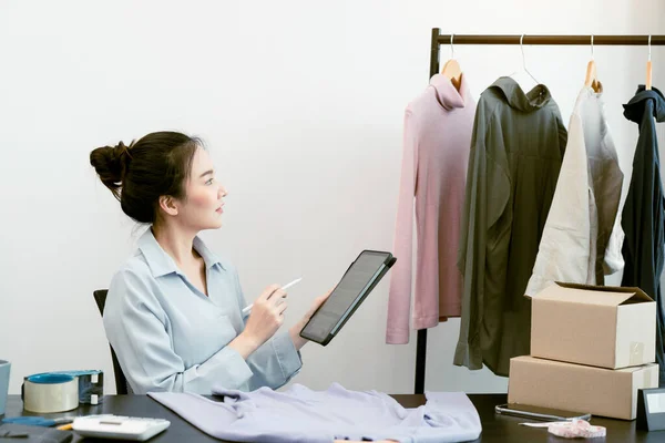 아시아 기업가가 태블릿을 창고에 옷들을 확인하고 있습니다 — 스톡 사진
