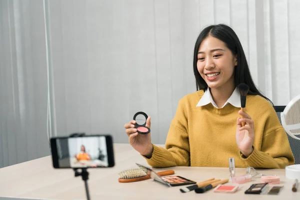 若いアジアの女性は 彼女のビデオカメラとテーブルの上の化粧品スキンケア製品についてVloggingと彼女のオンラインブログチャンネルのための製品の使用とレビューを実証します — ストック写真
