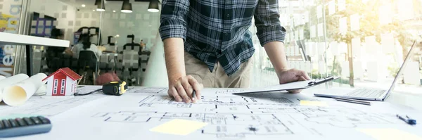 Interior designer or architect reviewing blueprints and holding pencil drawing on desk at home office.