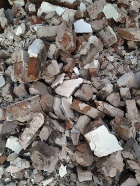Kırık kırmızı tuğlalar ve beton parçaları. Yıkılmış bir binanın enkazı. İnşaat alanında büyük beton ve taş atığı var.