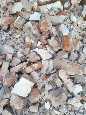 Kırık kırmızı tuğlalar ve beton parçaları. Yıkılmış bir binanın enkazı. İnşaat alanında büyük beton ve taş atığı var.