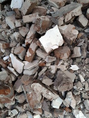 Kırık kırmızı tuğlalar ve beton parçaları. Yıkılmış bir binanın enkazı. İnşaat alanında büyük beton ve taş atığı var.
