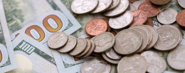 Masada düzensiz bir şekilde düzenlenmiş 100 dolarlık banknotların üzerinde büyük miktarda Amerikan sikkesi var. Para ve iş konsepti