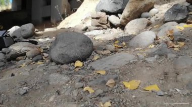 İnsansız hava aracı pis, dengesiz nehir kıyısına iniyor. Pervane yıkama yerinden taş ve toprak fırlatıyor..
