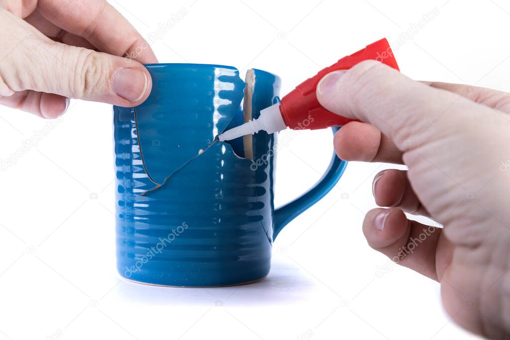 Hand holding a broken piece while applying glue to a hole in a cup