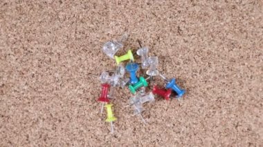 Spinning pile of multicolored red blue yellow green and clear tacks on a cork board