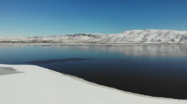 Pan left drone flight over frozen lake bed and icy shores