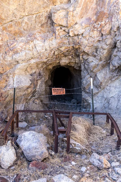 Mine entrance barred by warnbing sign on a barbed wire fence and a rusty metal structure in the Nevada desert