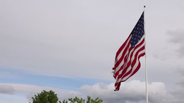 Large american flag flying in slow motion on a windy day over thick white clouds.