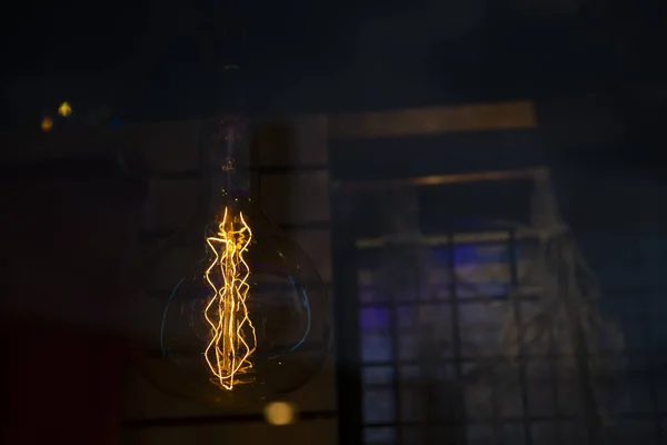 Edison globe shaped light bulb visible orange filaments over a dark background